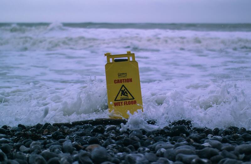 A 'Caution Wet Floor' Sign in crashing waves - photo by Oscar Sutton on Unsplash.com